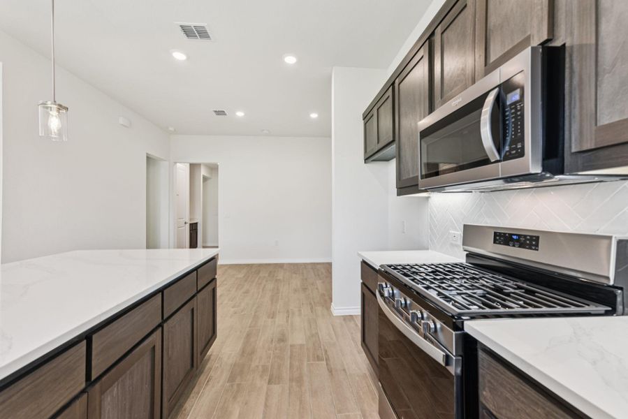 Kitchen featuring appliances with stainless steel finishes, dark brown cabinetry, recessed lighting, light stone countertops, and decorative light fixtures Kitchen featuring appliances with stainless steel finishes, dark brown cabinetry, recessed lighting, light stone countertops, and decorative light fixtures