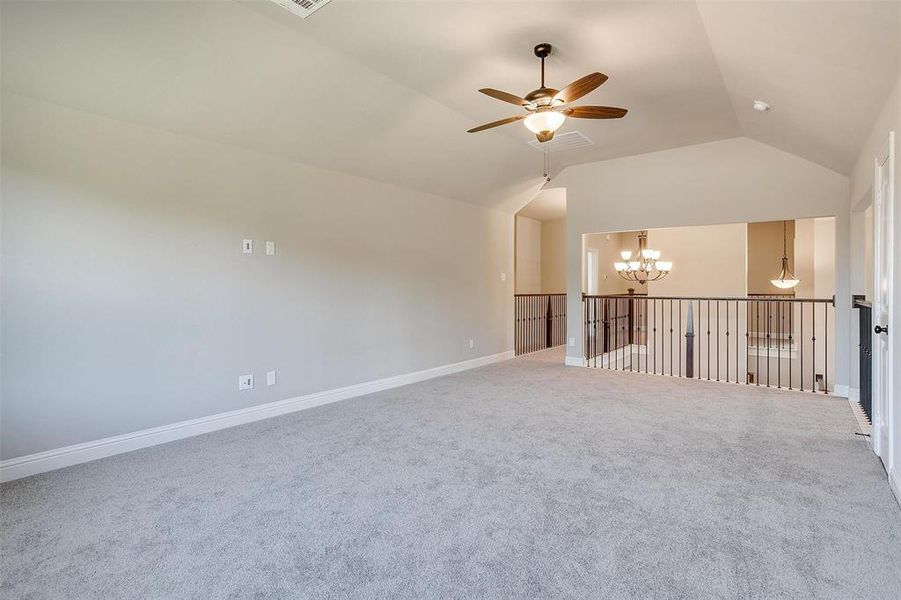 Empty room with carpet flooring, lofted ceiling, and ceiling fan with notable chandelier