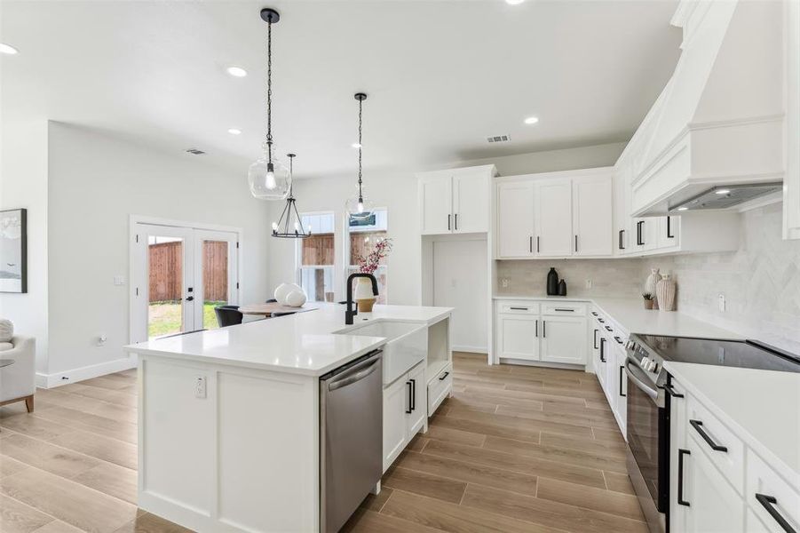 Kitchen featuring backsplash, dishwasher, sink, an island with sink, and electric range oven