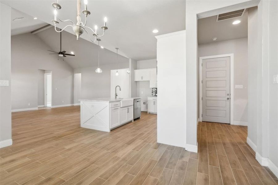 Kitchen featuring white cabinetry, ceiling fan with notable chandelier, an island with sink, light hardwood / wood-style floors, and decorative light fixtures