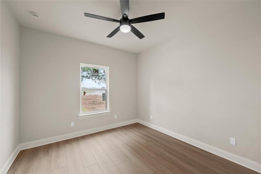 Neutral tone walls with white trim, wood-finish flooring, and a modern black ceiling fan with integrated lighting