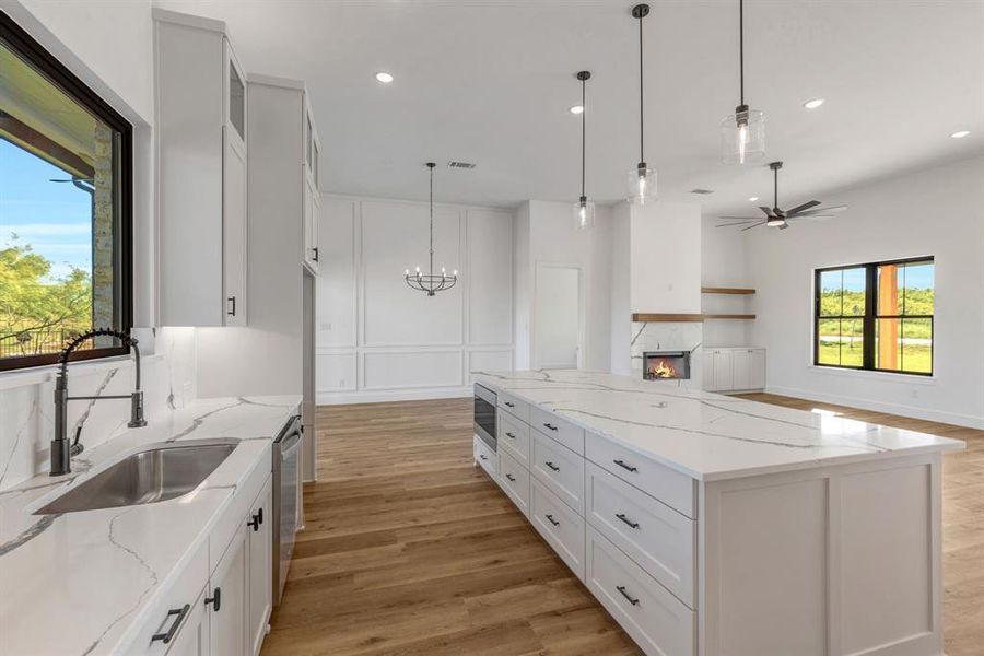 Kitchen with light stone countertops, a lit fireplace, a kitchen island, light wood finished floors, and white cabinets