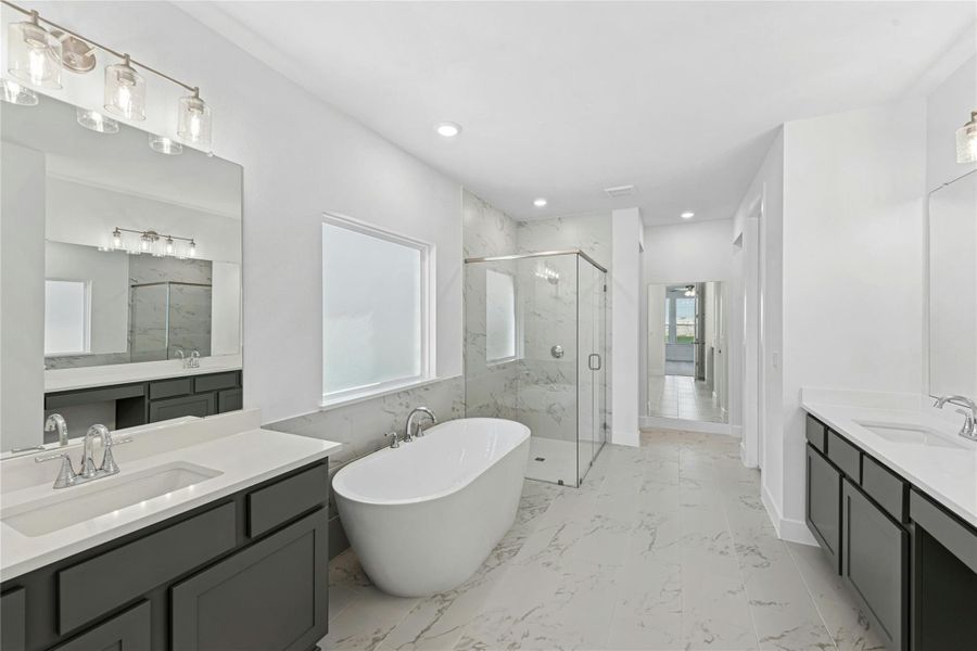 Full bath featuring a marble finish shower, two vanities, a soaking tub, light marble finish flooring, and recessed lighting