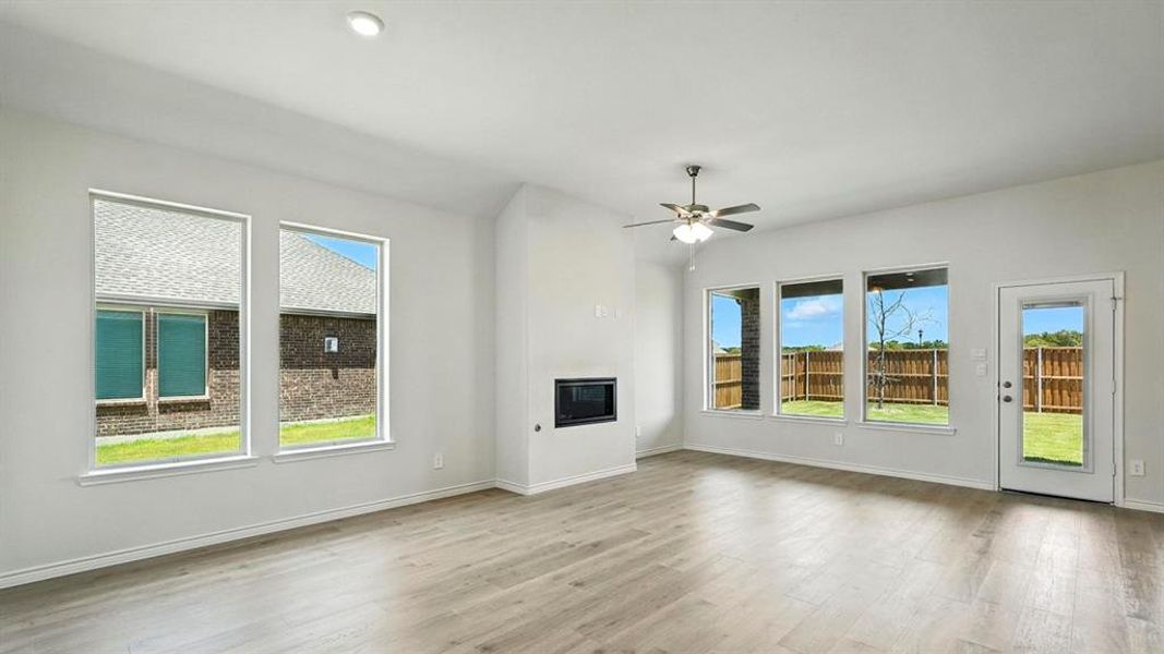 Spacious living area featuring light wood-finish flooring, a contemporary fireplace, and multiple large windows Spacious living area featuring light wood-finish flooring, a contemporary fireplace, and multiple large windows