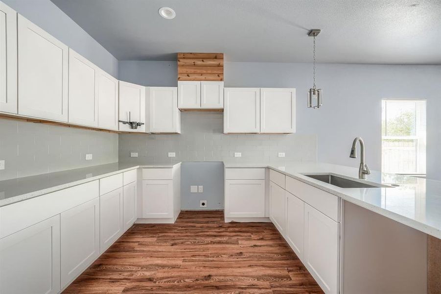 Kitchen featuring tasteful backsplash, white cabinets, pendant lighting, hardwood / wood-style flooring, and sink