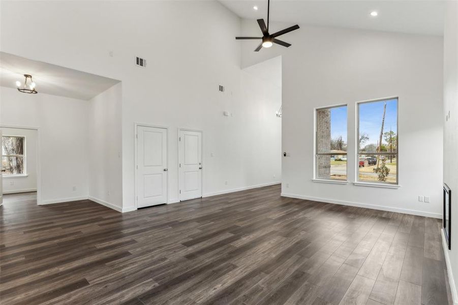 Unfurnished living room featuring dark wood-type flooring, ceiling fan, lofted ceiling, and a wealth of natural light