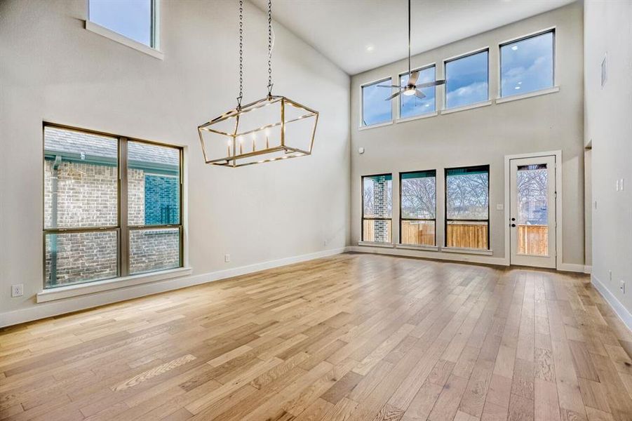 Unfurnished living room featuring light wood-type flooring, a ceiling fan, a high ceiling, and hanging lights
