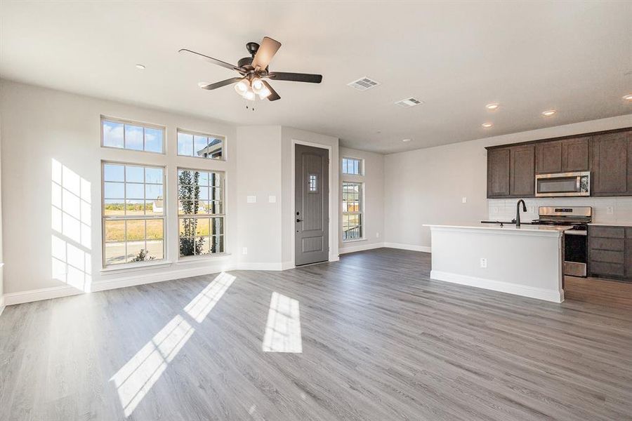 Kitchen featuring hardwood / wood-style flooring, dark brown cabinets, stainless steel appliances, a center island with sink, and ceiling fan