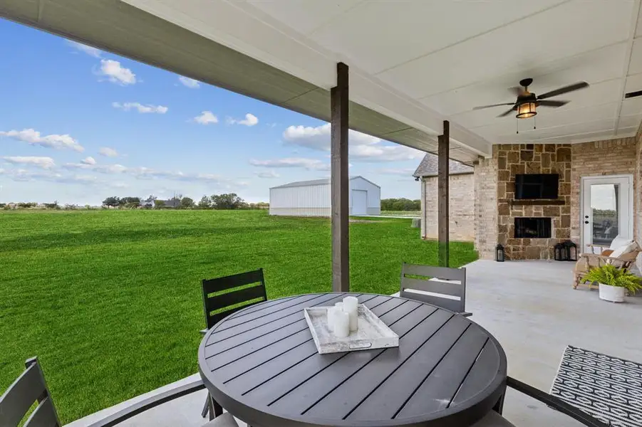 Covered outdoor patio with a stone-clad fireplace and ceiling fan