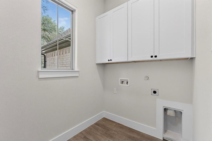 Dedicated utility area featuring white shaker-style cabinetry with matte black hardware, wood-finish flooring, and a single window with white trim