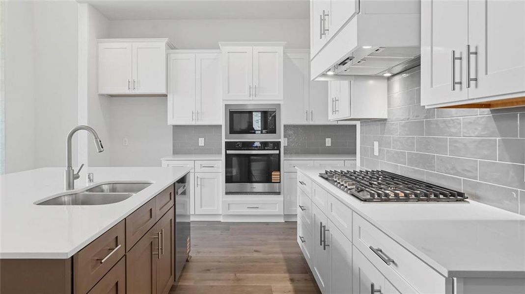Kitchen featuring stainless steel appliances, two tone color scheme, an island with sink, tasteful backsplash, and light wood finished floors