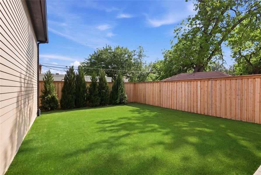 Expansive backyard featuring artificial turf, a new wood privacy fence, and mature evergreen trees Expansive backyard featuring artificial turf, a new wood privacy fence, and mature evergreen trees