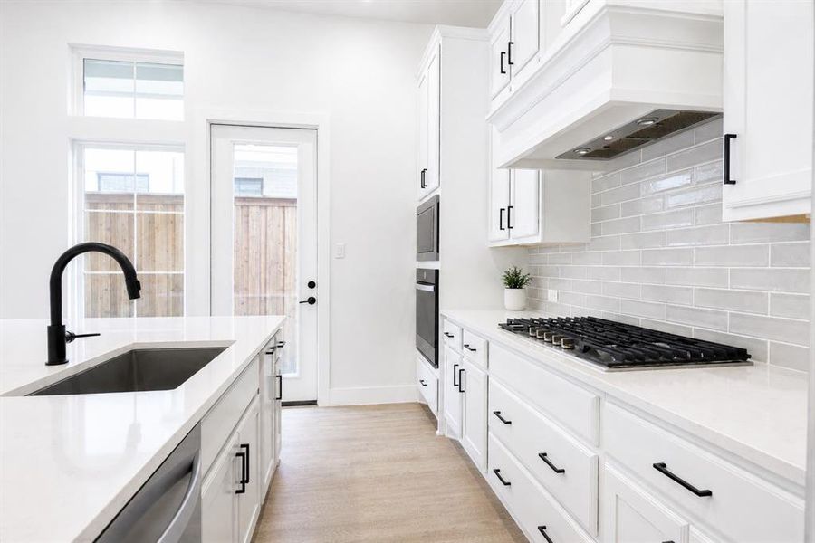 Kitchen featuring white cabinetry, light-toned wood-finish flooring, a stainless steel undermount sink with a matte black faucet, and a gas cooktop