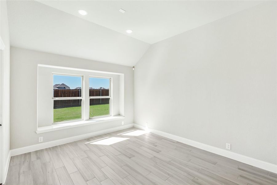 Empty bedroom with vaulted ceiling, light wood floors, and double window overlooking backyard Empty bedroom with vaulted ceiling, light wood floors, and double window overlooking backyard