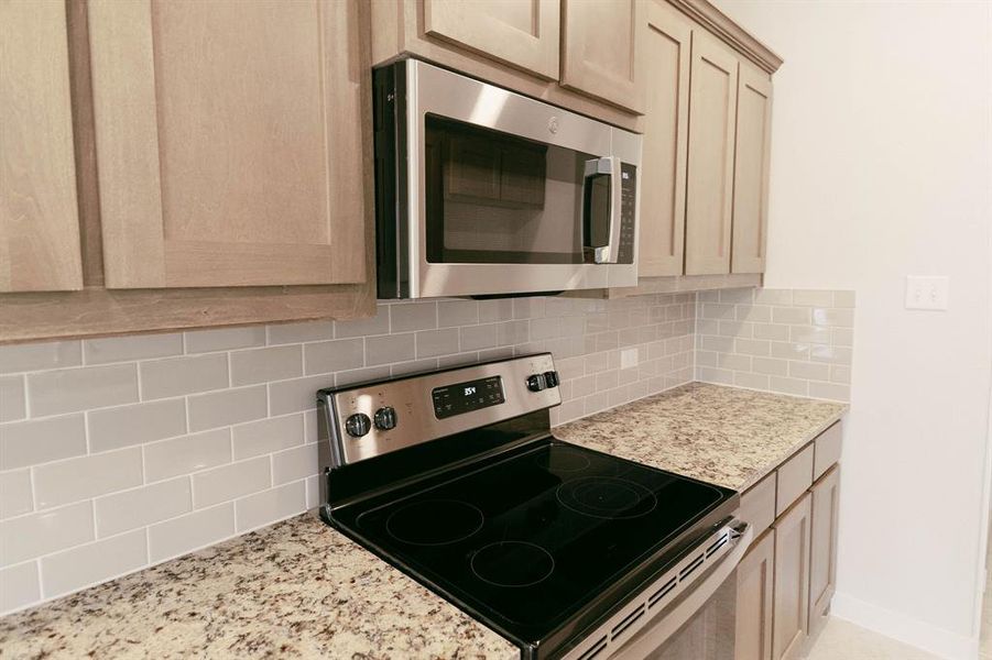 Kitchen with appliances with stainless steel finishes, light stone counters, and backsplash