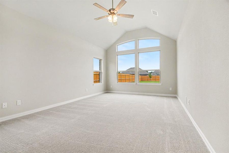 Spacious room featuring vaulted ceilings, light-toned carpeting, a multi-pane arched window, an additional single window, and a ceiling fan with integrated lighting Spacious room featuring vaulted ceilings, light-toned carpeting, a multi-pane arched window, an additional single window, and a ceiling fan with integrated lighting