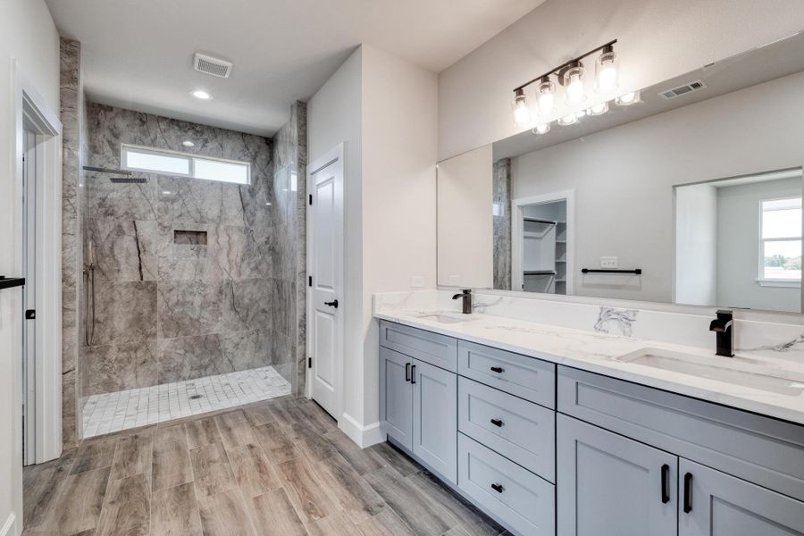Bathroom featuring a marble finish shower, double vanity, healthy amount of natural light, and wood finished floors