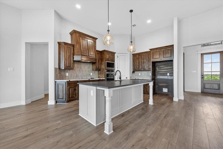 Kitchen featuring a breakfast bar, an island with sink, decorative light fixtures, light wood-style flooring, and two tone color scheme