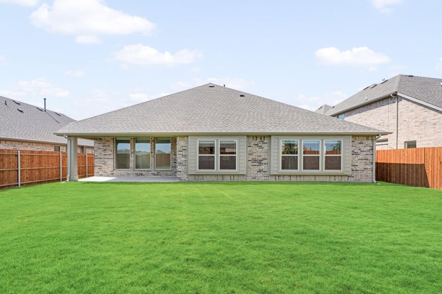 Rear view of single-story brick home with large backyard, wood privacy fence, and covered patio