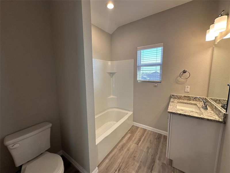 Full bathroom with vanity, shower / tub combination, lofted ceiling, hardwood / wood-style flooring, and toilet