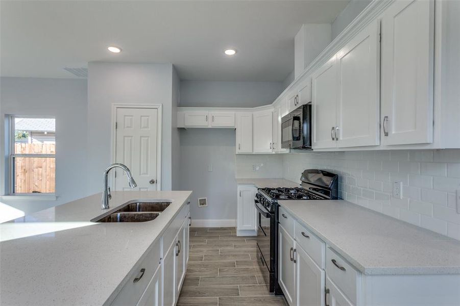 Kitchen featuring light stone countertops, white cabinetry, sink, black gas range oven, and light hardwood / wood-style floors