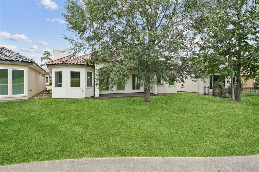 This is a single-story home with a tile roof and stucco exterior, featuring multiple windows for natural light. It's set on a well-maintained lawn with mature trees, offering both shade and curb appeal. A fenced backyard hints at privacy and security.