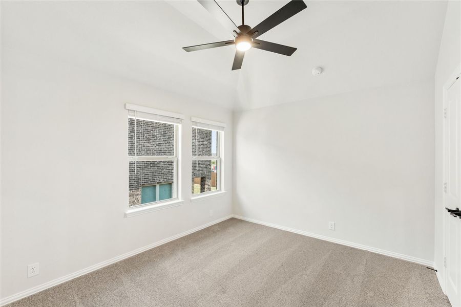 Empty bedroom with vaulted ceiling, ceiling fan, carpet flooring, and two windows Empty bedroom with vaulted ceiling, ceiling fan, carpet flooring, and two windows