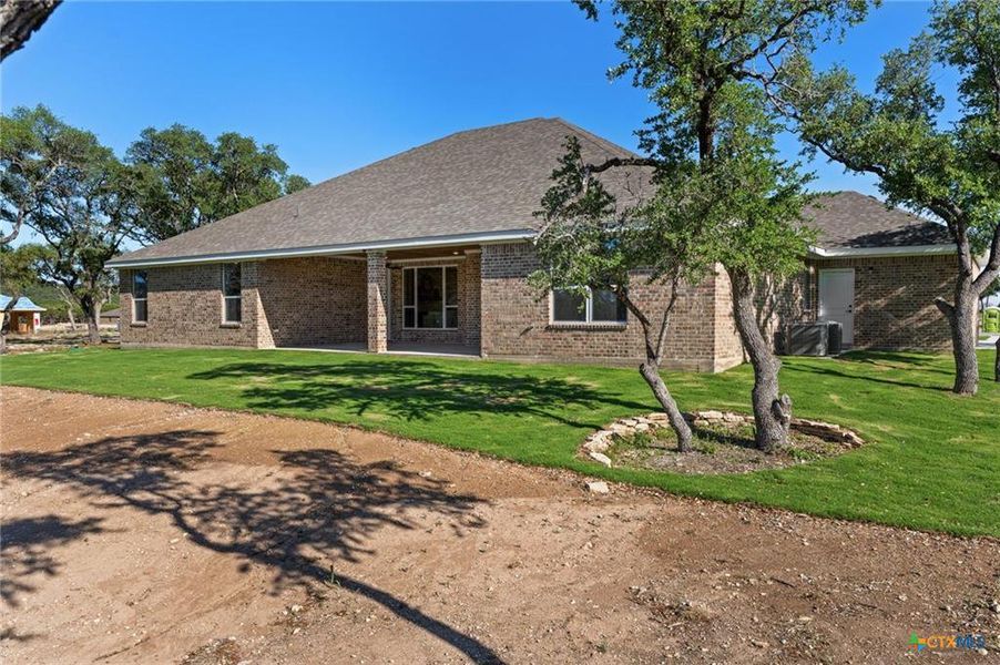 Back of property featuring a lawn, a patio, brick siding, and roof with shingles