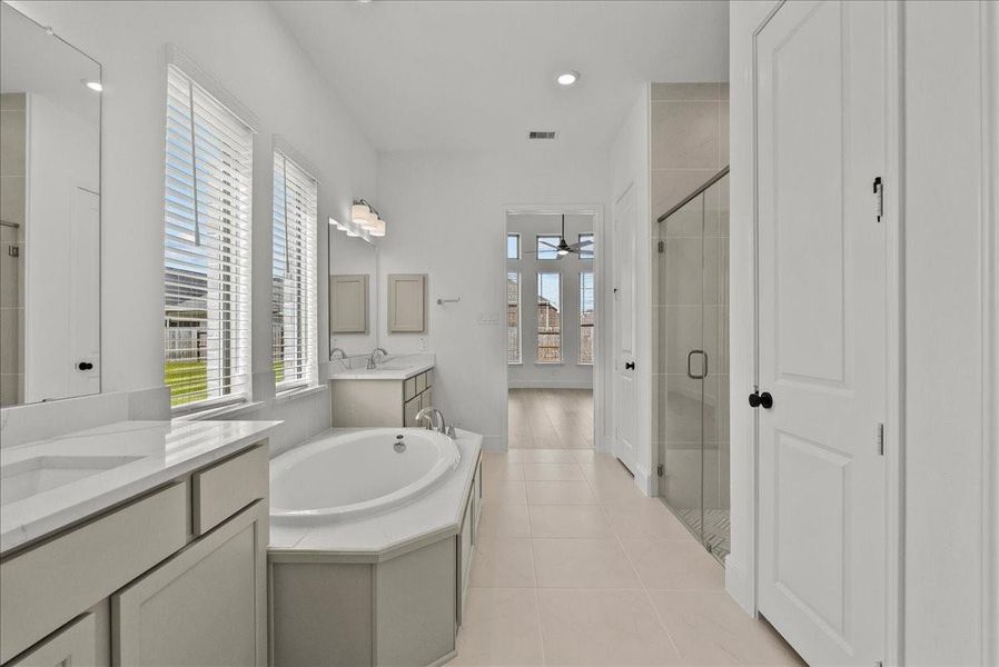 Spa-like en-suite bath with dual vanities, a walk-in shower, soaking tub, and large walk-in closet