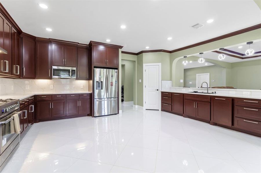 Spacious modern kitchen featuring sleek dark wood cabinetry, stainless steel appliances, and a large countertop with ample storage. The glossy white floor tiles and elegant lighting create a bright, inviting atmosphere.