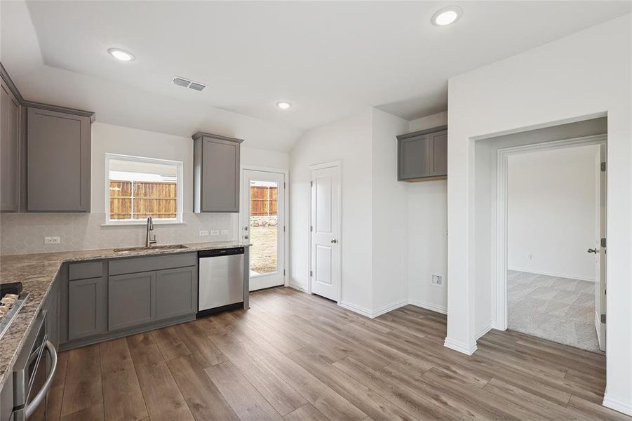 Kitchen featuring gray cabinets, stainless steel appliances, light stone countertops, recessed lighting, and lofted ceiling