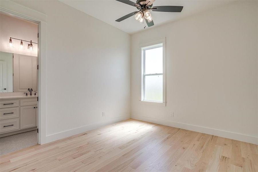 Unfurnished bedroom featuring light wood finished floors, a sink, ensuite bathroom, and baseboards