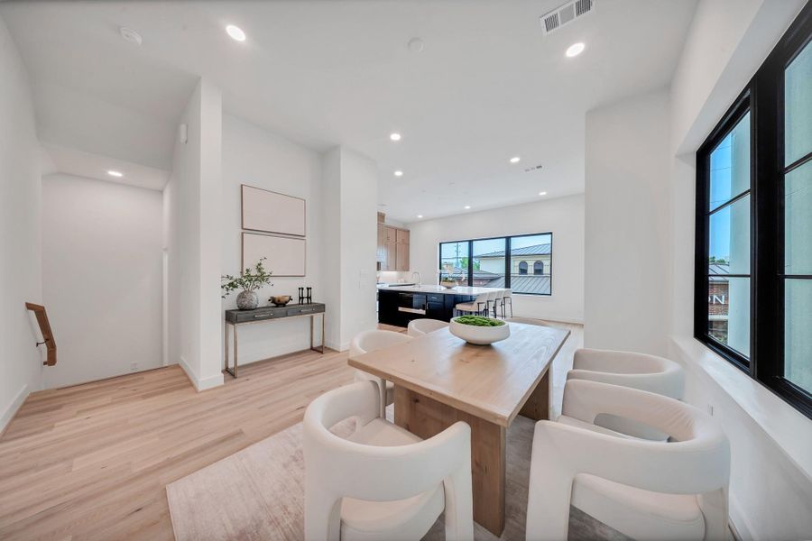 Dining area with a wooden table and modern white chairs. Large windows provide ample natural light, while light wood flooring and minimalist decor create an airy, contemporary feel. Dining area with a wooden table and modern white chairs. Large windows provide ample natural light, while light wood flooring and minimalist decor create an airy, contemporary feel.