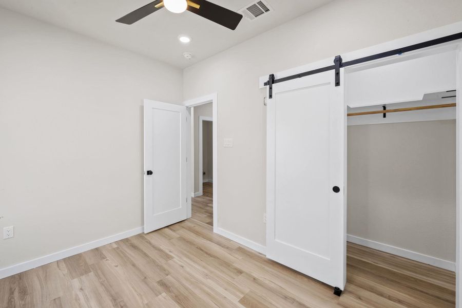 Unfurnished bedroom with a barn door, light wood-style floors, ceiling fan, a closet, and recessed lighting Unfurnished bedroom with a barn door, light wood-style floors, ceiling fan, a closet, and recessed lighting