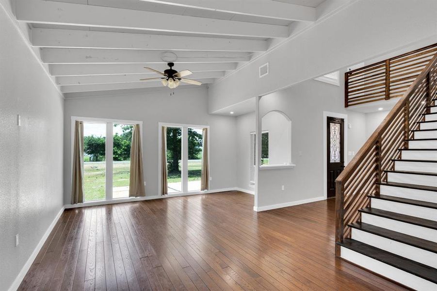 Unfurnished living room with baseboards, hardwood / wood-style flooring, ceiling fan, and stairway