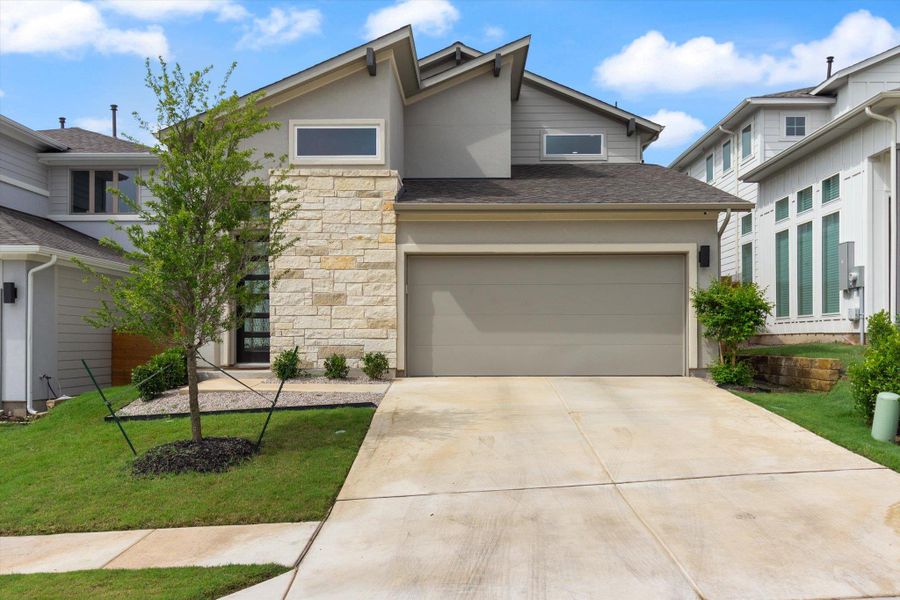 View of front of house with stone siding, concrete driveway, a front lawn, roof with shingles, and stucco siding