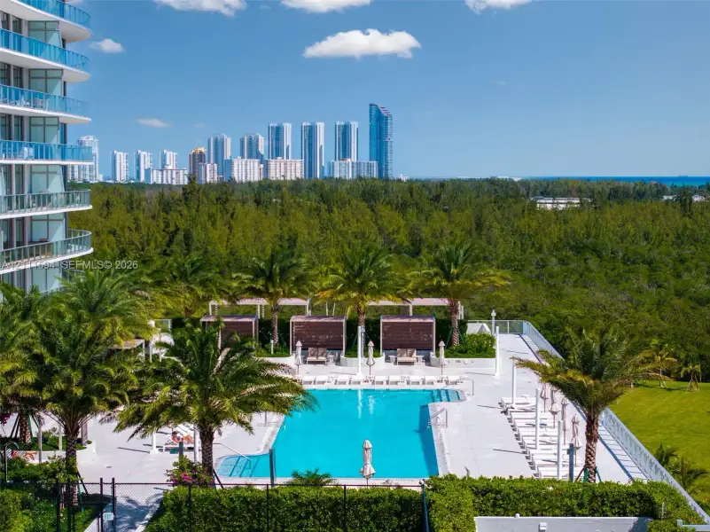 Swimming pool with concrete decking, perimeter privacy hedging, mature palm trees, and elevated cabanas Swimming pool with concrete decking, perimeter privacy hedging, mature palm trees, and elevated cabanas