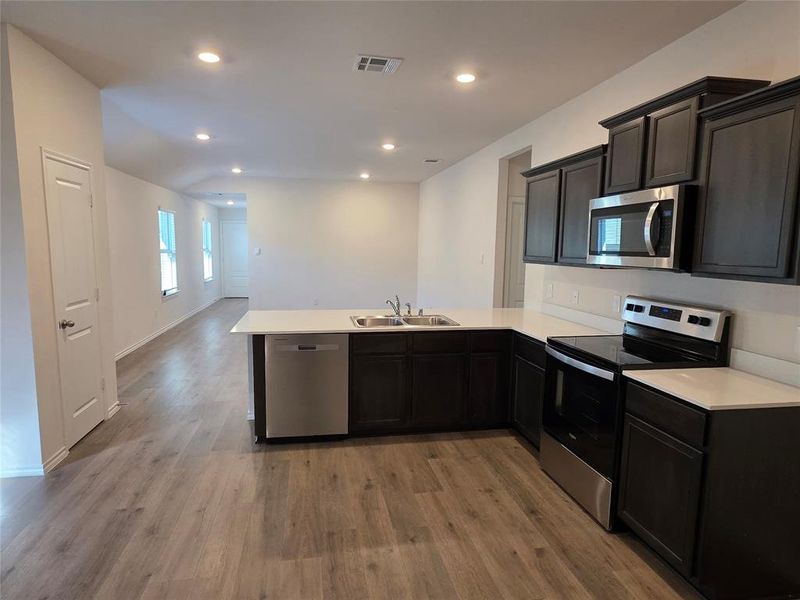 Kitchen with appliances with stainless steel finishes, light countertops, a peninsula, dark wood-style floors, and recessed lighting Kitchen with appliances with stainless steel finishes, light countertops, a peninsula, dark wood-style floors, and recessed lighting