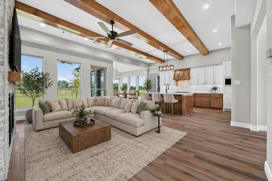 Open-concept living space with vaulted ceilings featuring exposed wood beams and wood-finish flooring