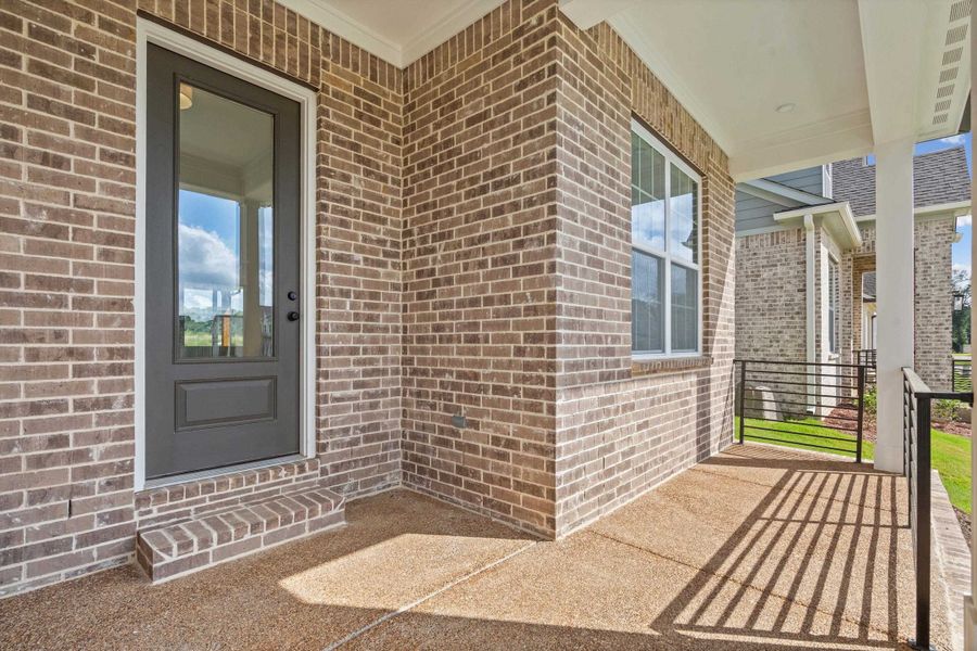 Brick exterior with a covered porch featuring an exposed aggregate concrete floor, white columns, and a black metal railing Brick exterior with a covered porch featuring an exposed aggregate concrete floor, white columns, and a black metal railing
