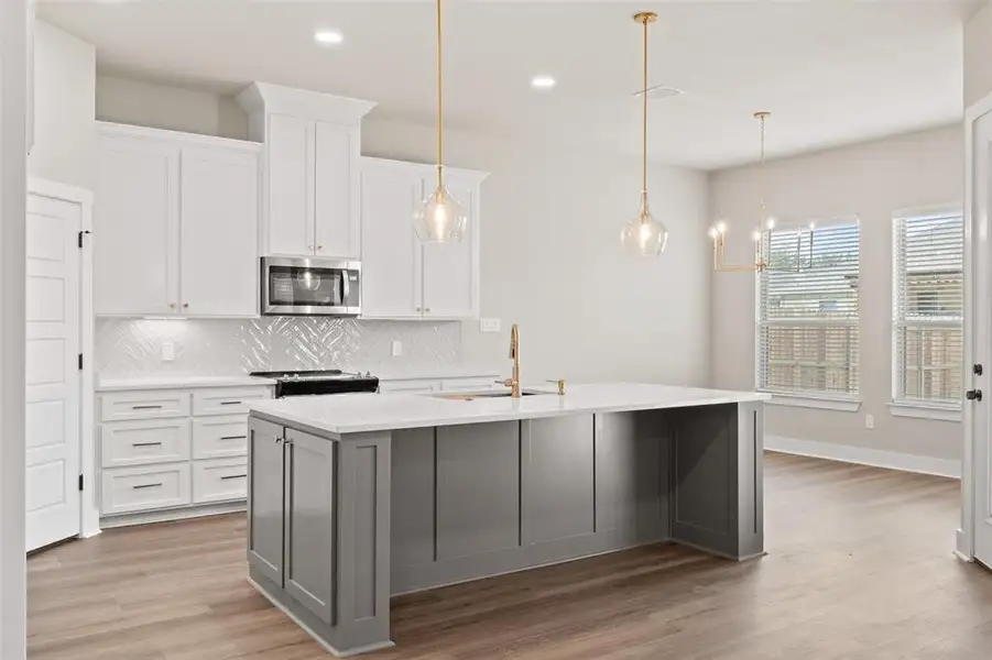 Kitchen with backsplash, light wood-style flooring, two tone cabinetry, a kitchen island with sink, and stainless steel microwave