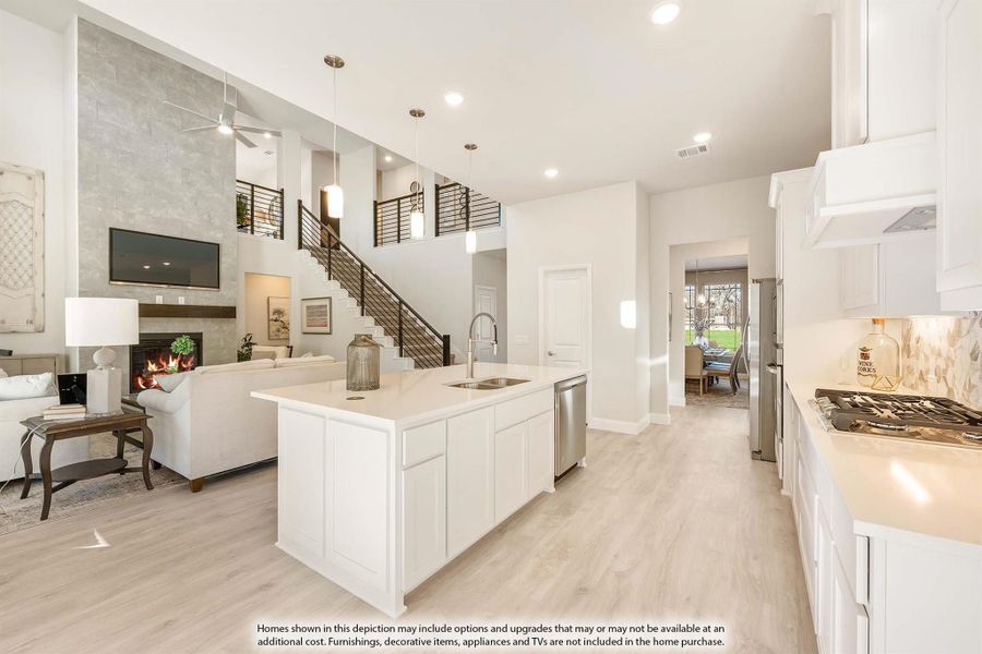 Open-concept kitchen with white island and cabinets, flowing into living room with two-story fireplace and staircase