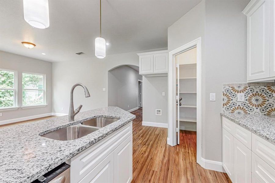 Kitchen with light stone counters, white cabinets, sink, light wood-type flooring, and hanging light fixtures