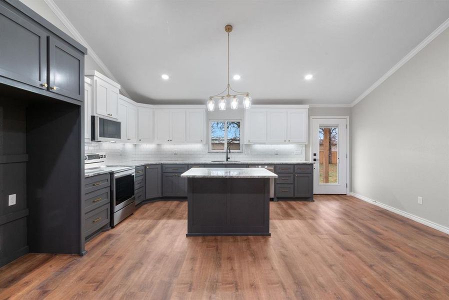 Kitchen featuring stainless steel electric range oven, a kitchen island, light stone counters, pendant lighting, and white cabinets Kitchen featuring stainless steel electric range oven, a kitchen island, light stone counters, pendant lighting, and white cabinets