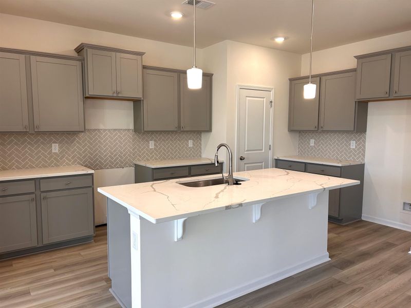 Kitchen with decorative light fixtures, gray cabinets, light stone countertops, a kitchen breakfast bar, and decorative backsplash