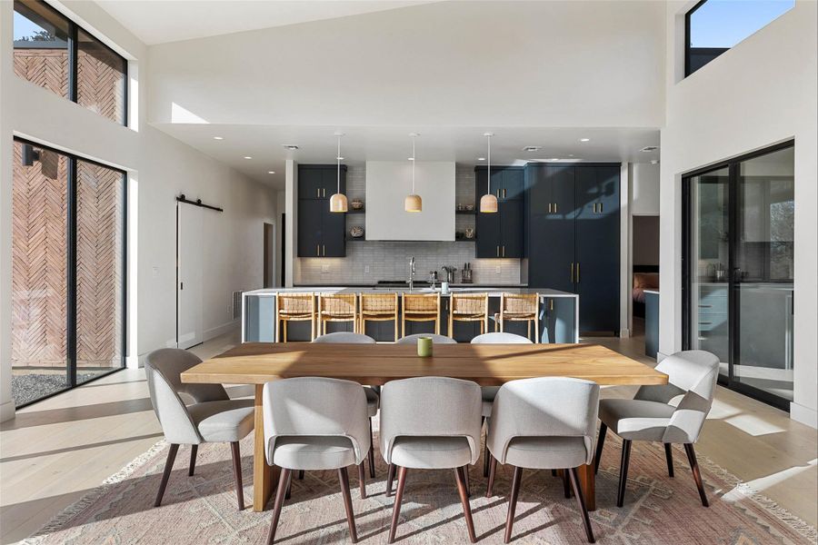 Kitchen featuring a towering ceiling, dark cabinets, modern cabinets, a center island with sink, and pendant lighting