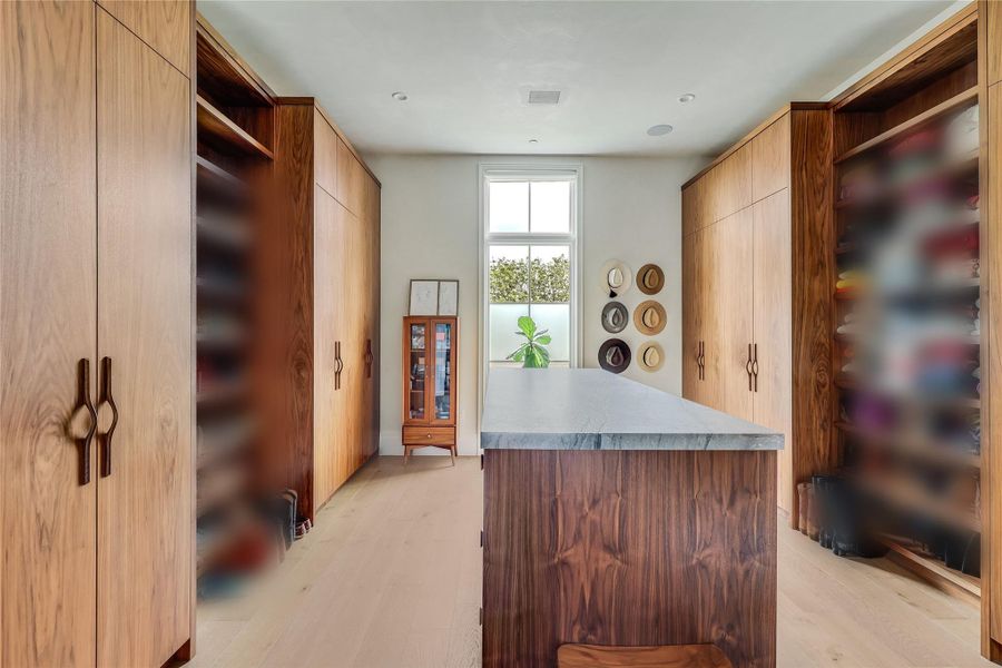 An organized walk-in closet boasts custom wood cabinetry and a central island with a quartzite top.