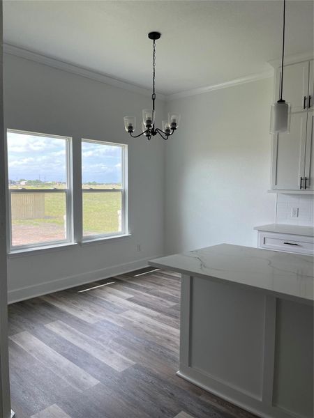 This photo showcases a bright dining area with large windows offering a view of the outdoors. The room features a modern light fixture, medium gray/wood water proof plank flooring, and a sleek kitchen island with Quartz countertops.