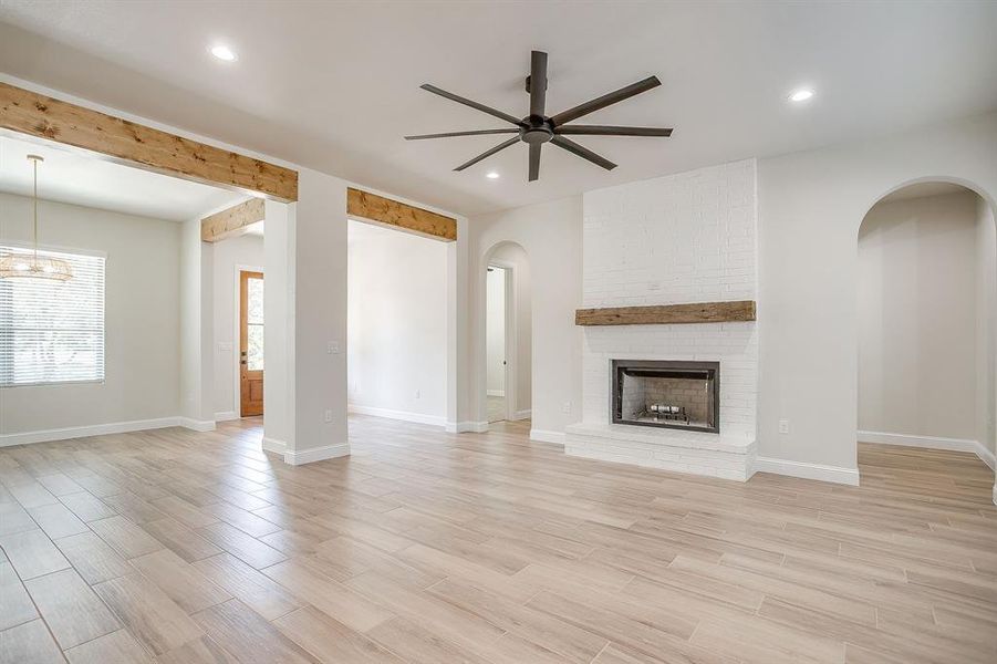 Unfurnished living room with light wood-style flooring, a brick fireplace, arched walkways, a ceiling fan, and recessed lighting Unfurnished living room with light wood-style flooring, a brick fireplace, arched walkways, a ceiling fan, and recessed lighting
