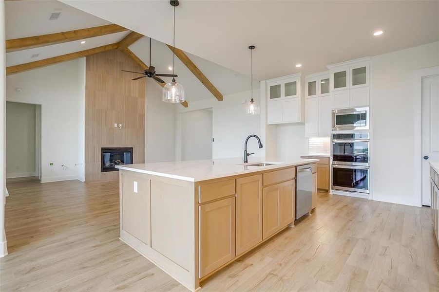 Kitchen with a tile fireplace, a kitchen island with sink, stainless steel appliances, sink, and ceiling fan